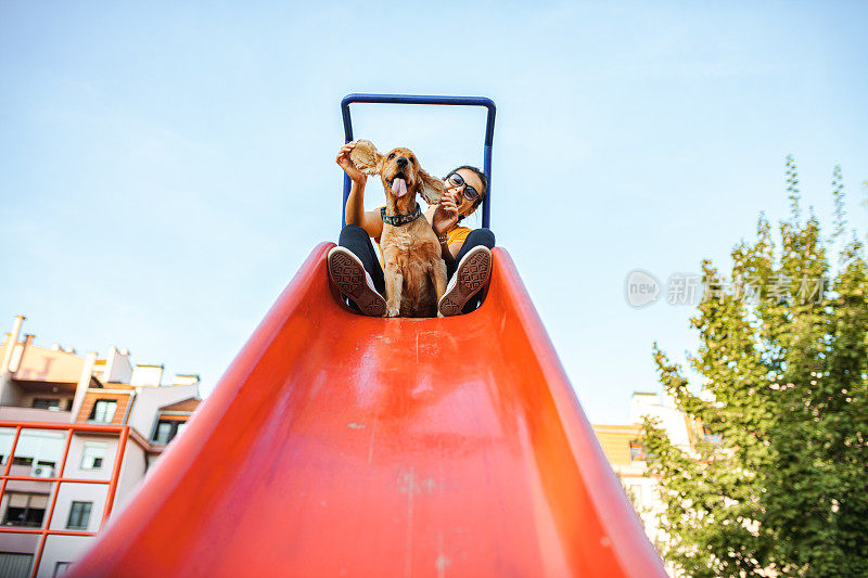 一个年轻的女人和她的狗在城市公园的红色滑梯上玩耍