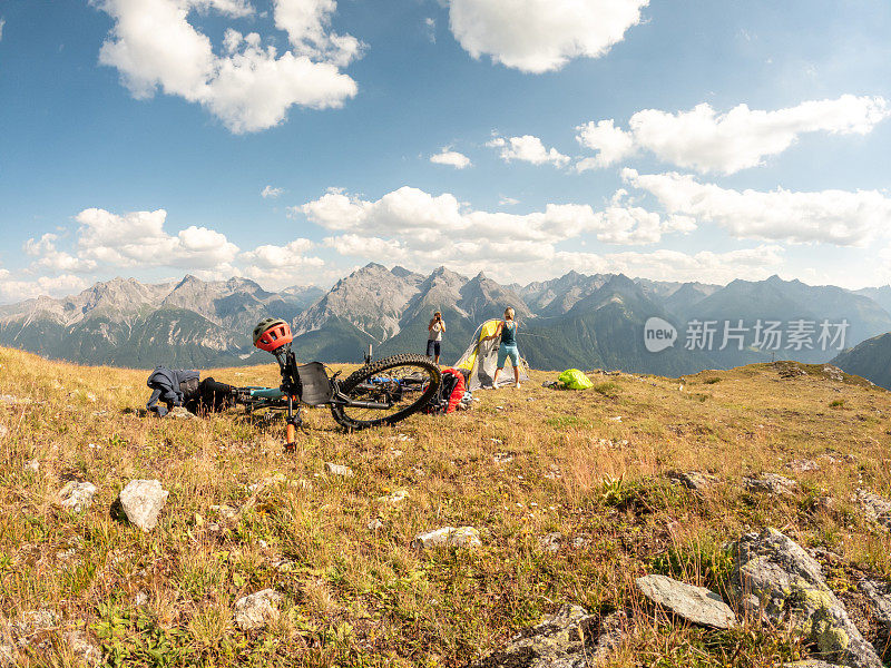 一对夫妇在瑞士阿尔卑斯山骑自行车，日落时分在山顶搭起帐篷