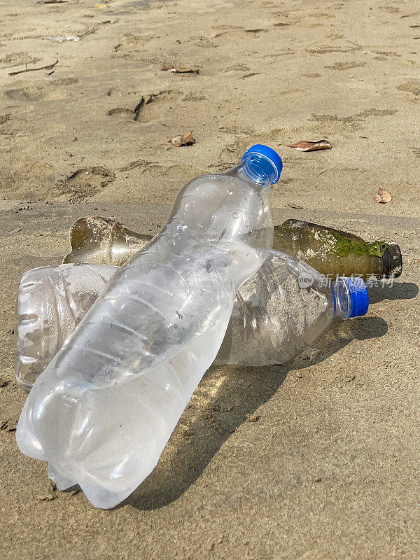 近景:退潮时被冲到沙滩上的三个塑料水瓶堆成一堆，海岸上的海洋垃圾和污染，乱扔的沙子，肮脏的海滩，聚焦于前景