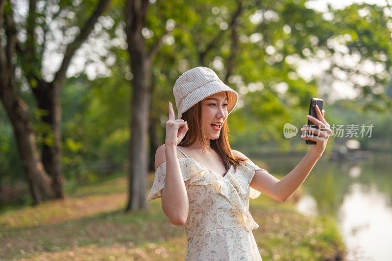 年轻的亚洲女子在公园用手机自拍。在郁郁葱葱的绿色森林里，美女视频通话