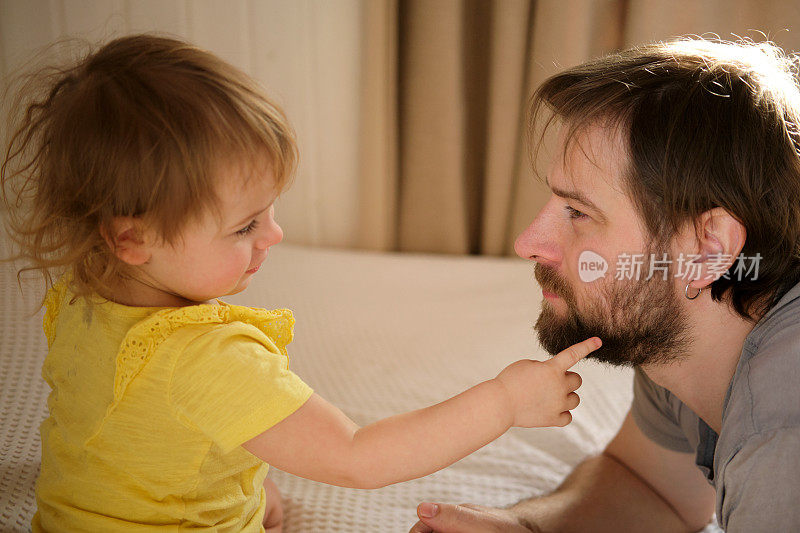 快乐的父亲和女儿，小女孩。一岁的婴儿微笑着，大笑着，抬头看着爸爸。男人对孩子示爱。坦诚的真实情感。胡子爸爸和小孩。正宗的家庭生活方式。