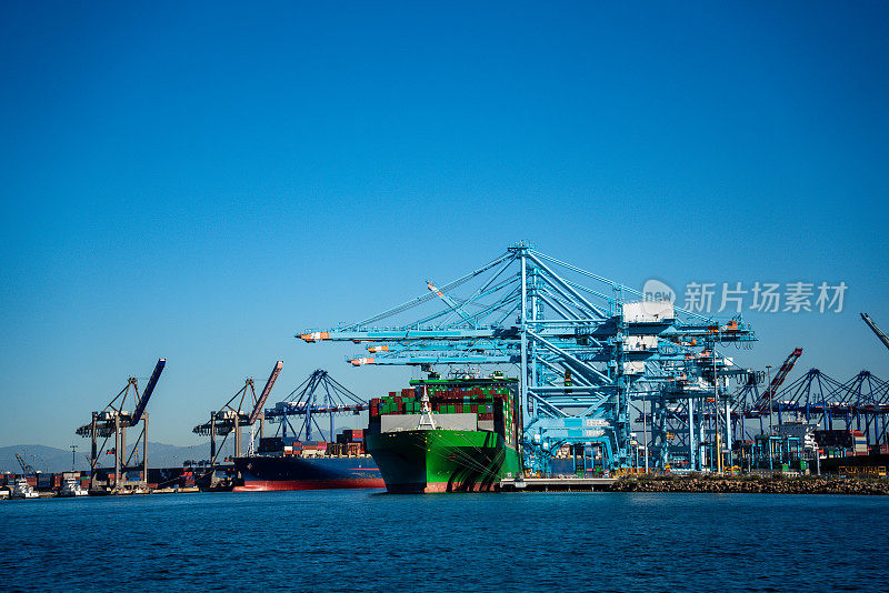 一队巨大的货船挤满了洛杉矶港口，它们巨大的框架使周围的基础设施相形见绌。它们满载着集装箱，象征着全球贸易的相互联系，热切地等待着下一次航行。