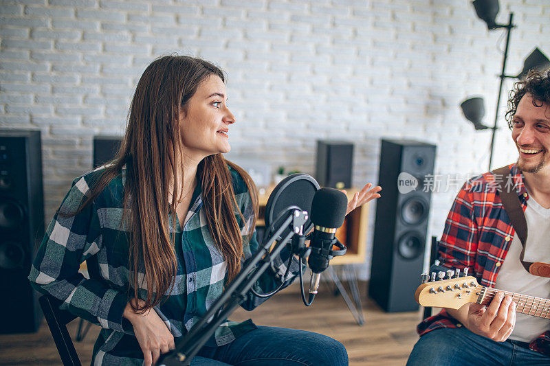 在家庭音乐录音室里，当吉他手弹吉他时，年轻女子对着麦克风唱歌
