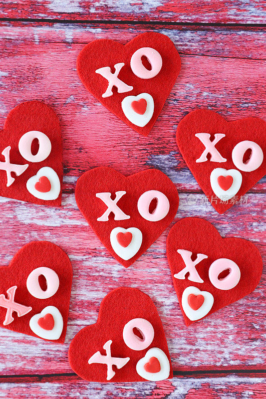 用x、o和糖霜心形装饰的红色毛毡心形特写图像，拥抱和亲吻，情人节装饰，粉红色木纹背景，高架视图，情人节和浪漫的概念