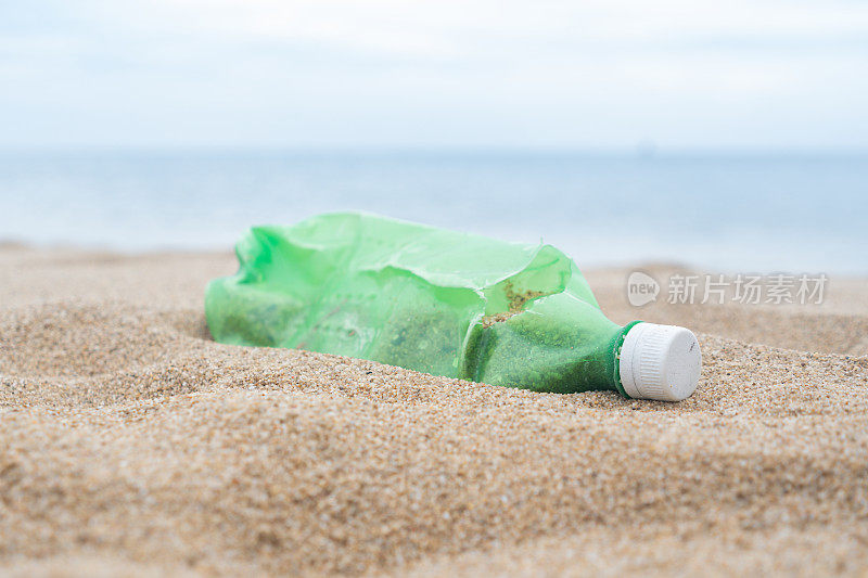 一个绿色的塑料瓶废物被丢弃在海滩上造成的人类活动导致海滩脏。乱扔塑料垃圾造成环境问题。