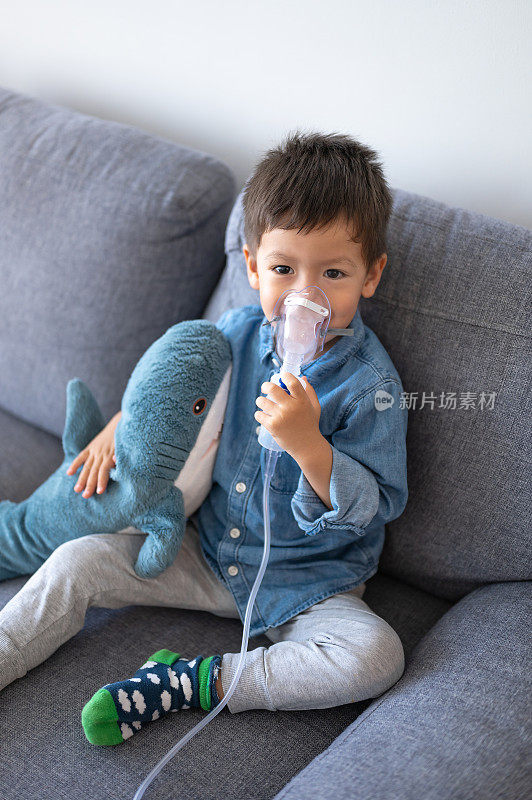 小男孩带着吸入雾化器坐在沙发上