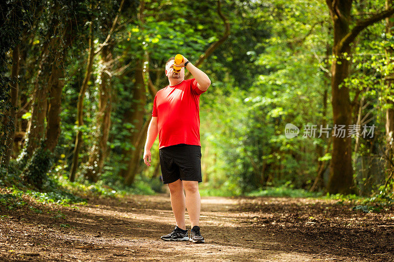 疲惫的男性慢跑者在森林小路上喝水