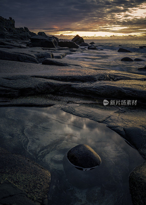 日落时海边巨大的圆形鹅卵石，背景是山脉。