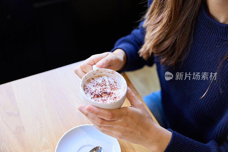 在咖啡桌端着卡布奇诺的女人特写