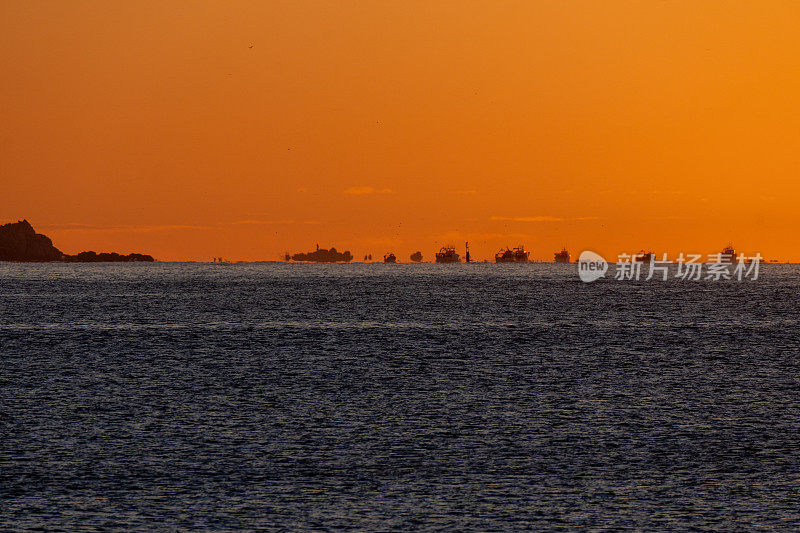 在地中海地平线上的渔船从Palamós的港口和海岸出发出海捕虾，被黎明的阳光照亮，形成了海市蜃楼和光学错觉。