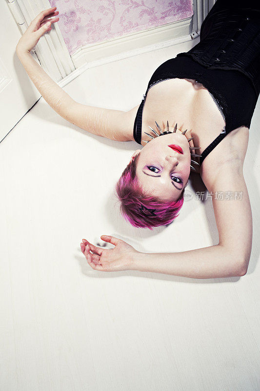年轻的粉红头发的女人躺在白色的地板上，肖像室内