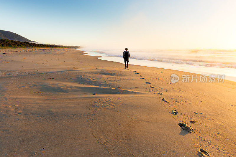日出时分，漫步在迷雾中的海滩上的人