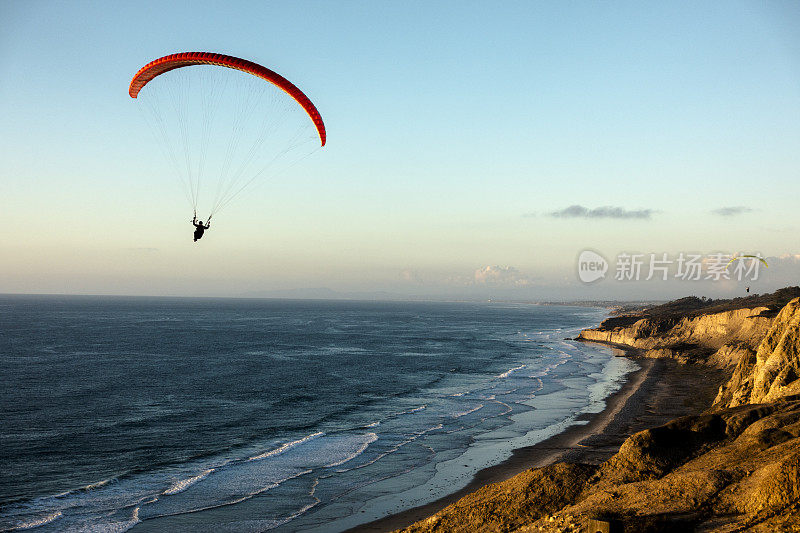 日落时，滑翔伞飞越海洋悬崖