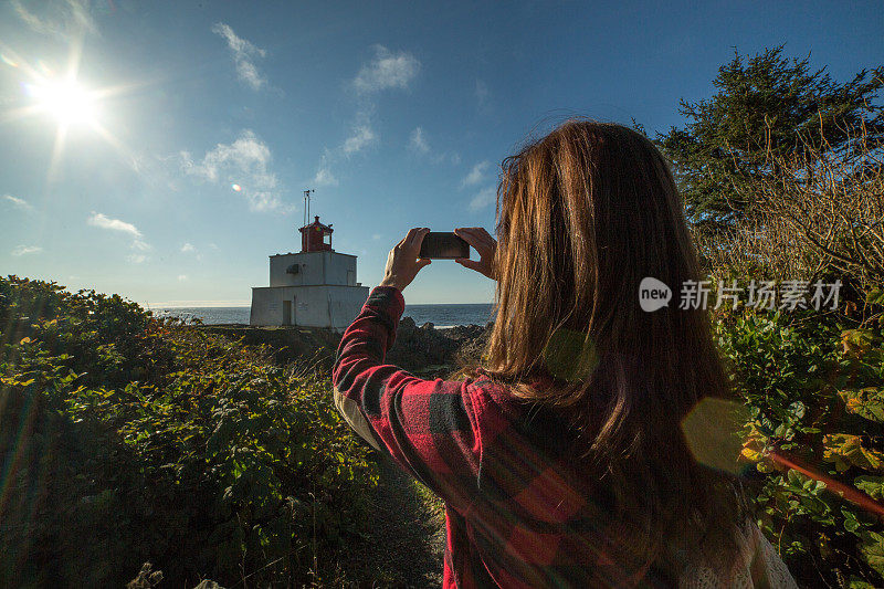 年轻女子用手机拍摄一座灯塔。