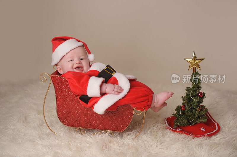 穿着圣诞老人服装坐在雪橇上的快乐婴儿