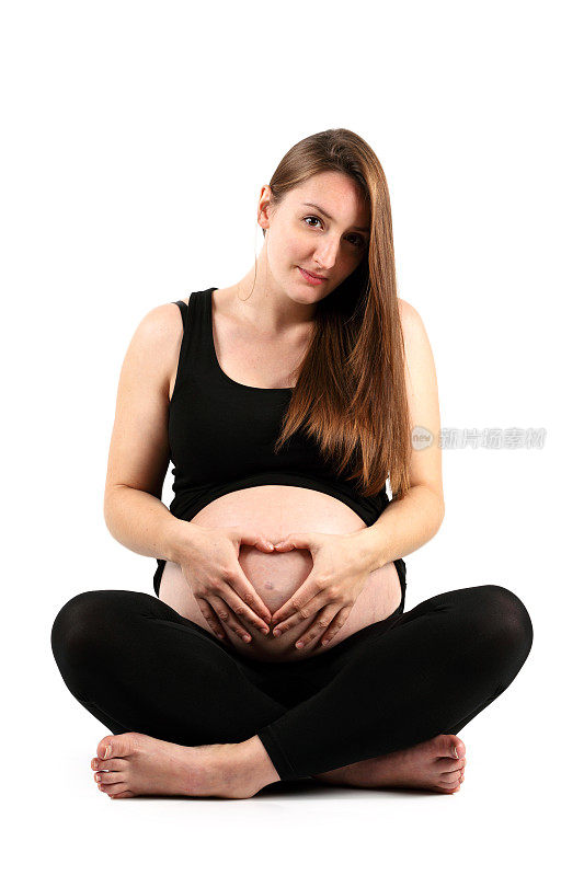 盘腿的年轻孕妇做心形手指