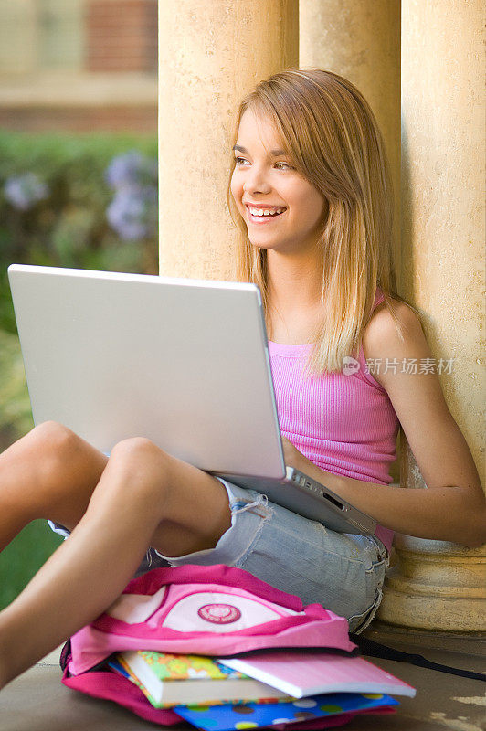 十几岁的女学生在校园里拿着书和笔记本电脑