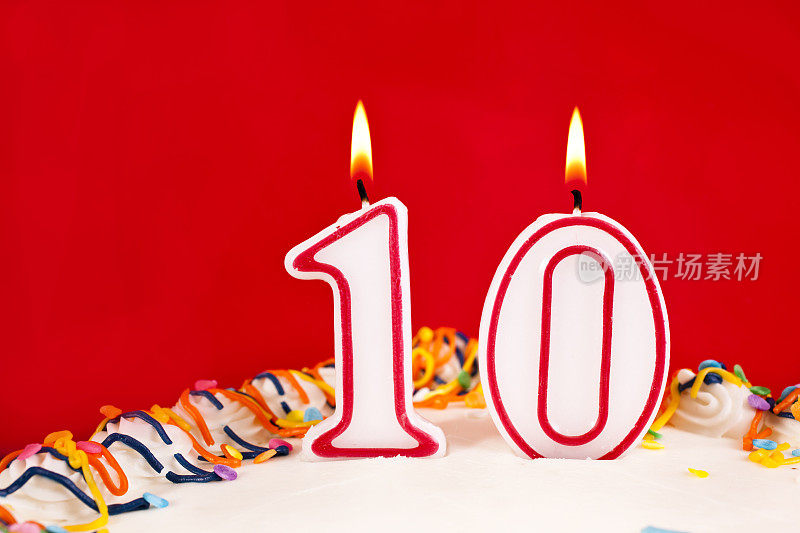 用10号燃烧的蜡烛装饰生日蛋糕。红色的背景