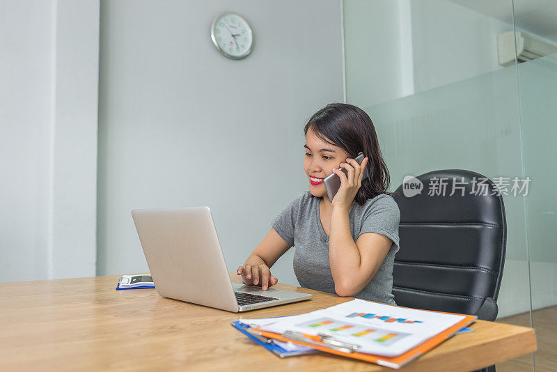 微笑的女人接听客户电话，同时工作在笔记本电脑上