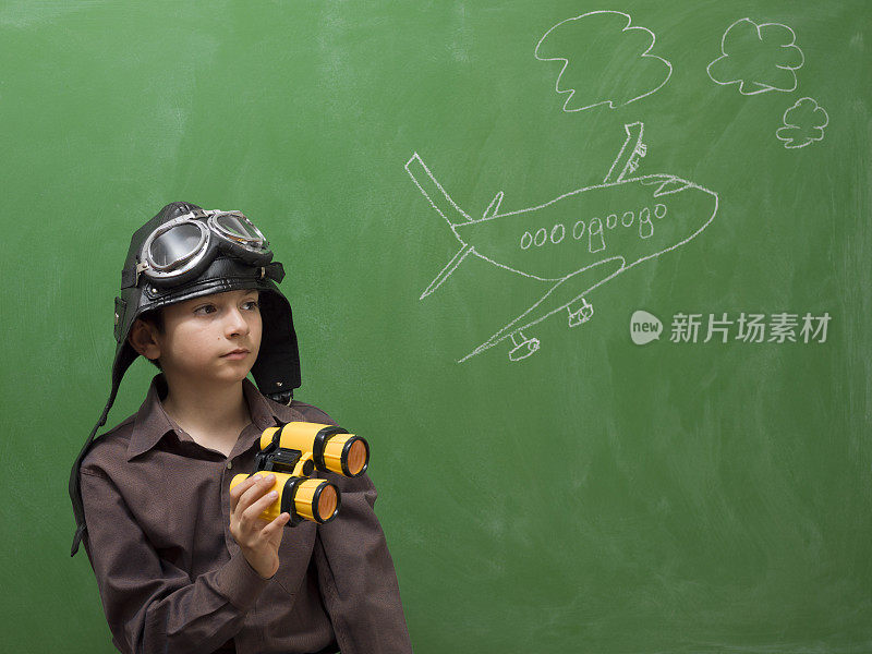 带着飞行镜的小男孩拿着望远镜站在黑板前