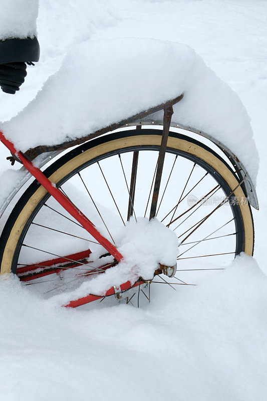 一辆红色旧自行车的后轮被雪覆盖