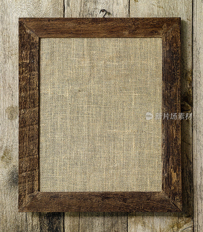 旧风化破旧的自然木制相框与粗麻布袋背景框在里面，在一个旧风化的木板墙背景。