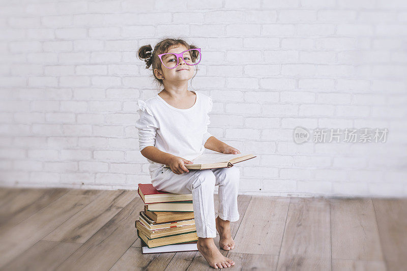 小女孩戴着眼镜坐在一堆书上