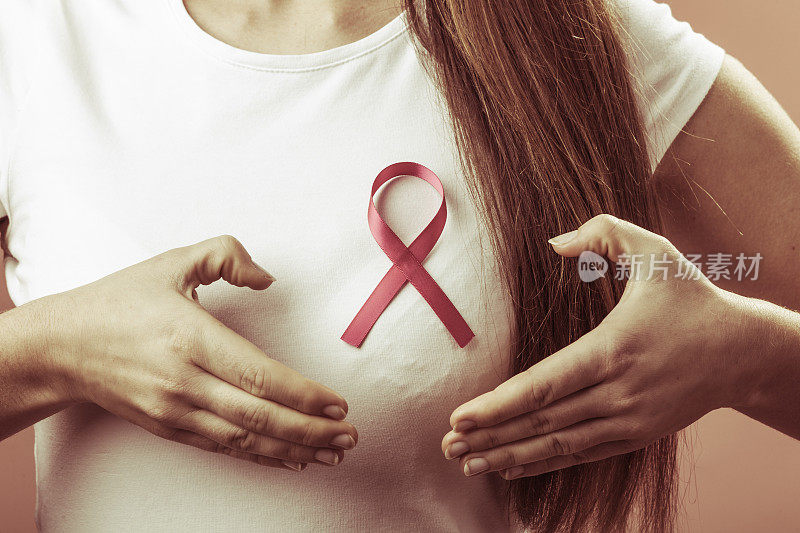 乳腺癌。女人的手在粉红色的丝带上做心形