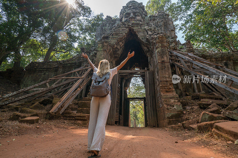 女旅人从寺庙的复杂大门伸出双臂，感受着旅行的自由和幸福