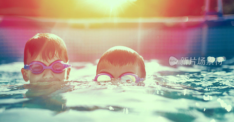 两个戴着护目镜的小孩在日落时在游泳池里游泳
