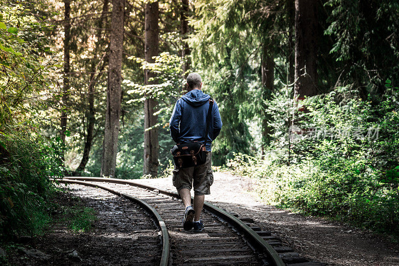 年轻的冒险男子独自走在铁路上在森林的后视图