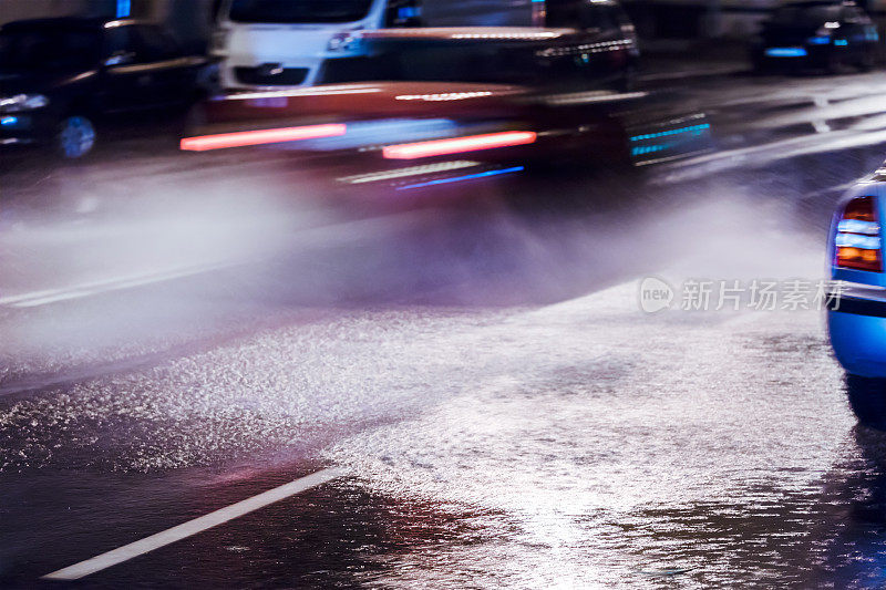 汽车在大雨中行驶，车轮溅起水花。城市夜晚的交通状况。