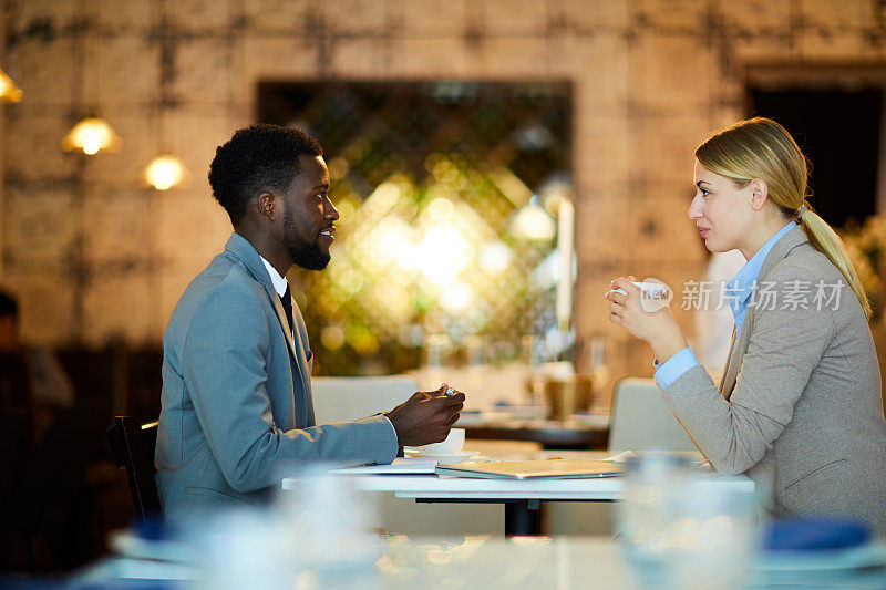 内容是自信的年轻商业伙伴穿着正装坐在桌边喝咖啡，在咖啡馆共进午餐