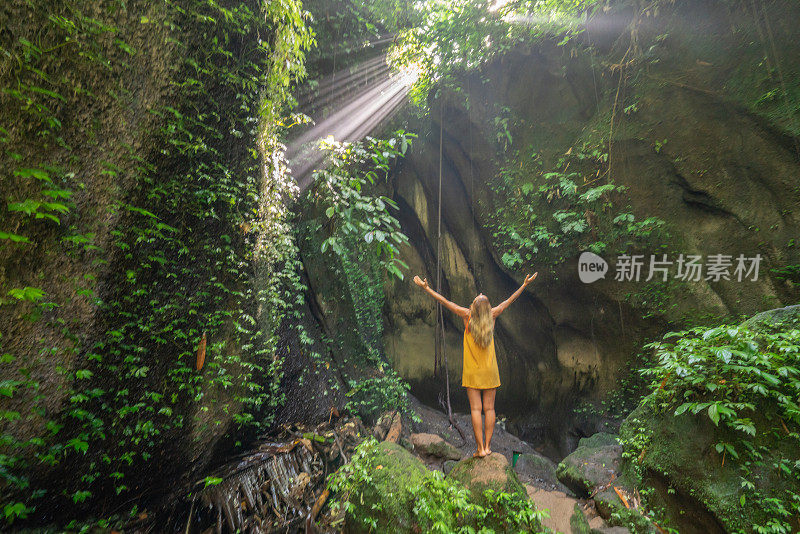 在巴厘岛的热带雨林中，旅行的年轻女子张开双臂拥抱大自然的美丽。人们以自然为旅游理念。