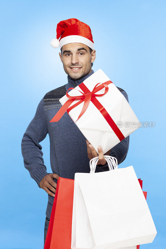 圣诞老人帽子人的肖像展示礼物，拿着购物纸袋。冬天的圣诞节。