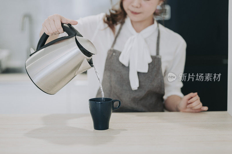 在厨房里，一位亚洲华裔女性正在往她的咖啡杯上倒热水