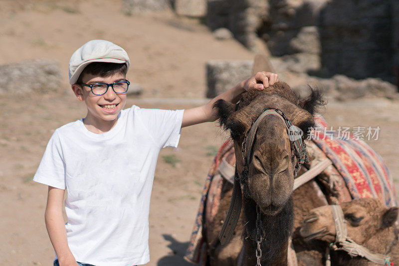 可爱的男孩和骆驼在沙漠里摆姿势