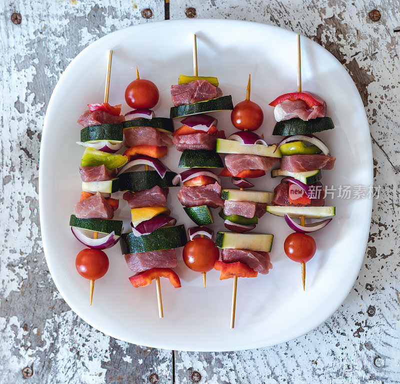 羊肉串，一种希腊菜，配上猪排和蔬菜，盘上串着烤肉，特写