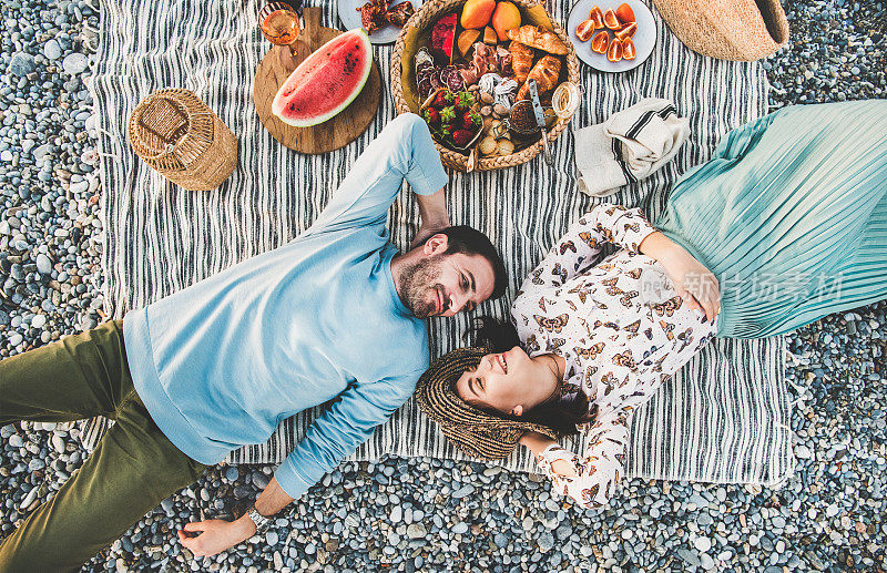 日落时分，一对年轻夫妇躺在毯子上野餐