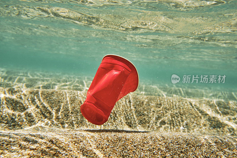 环境问题，红色塑料用的一次性塑料杯在海里。