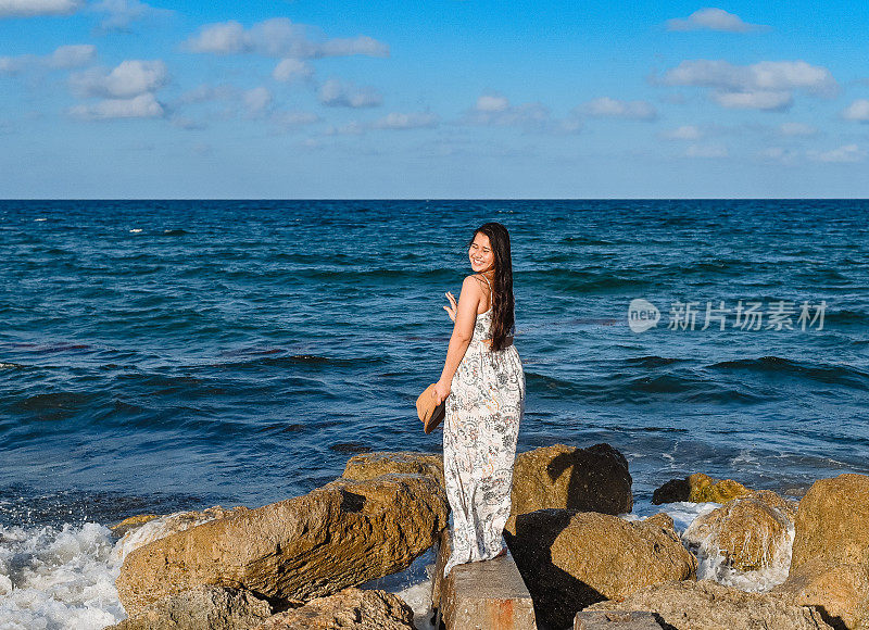 年轻漂亮的泰国裔柬埔寨裔美国妇女站在海边一块露出海面的岩石上