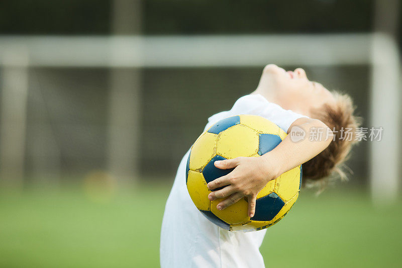 一个八岁的孩子拿着他的足球向上看。