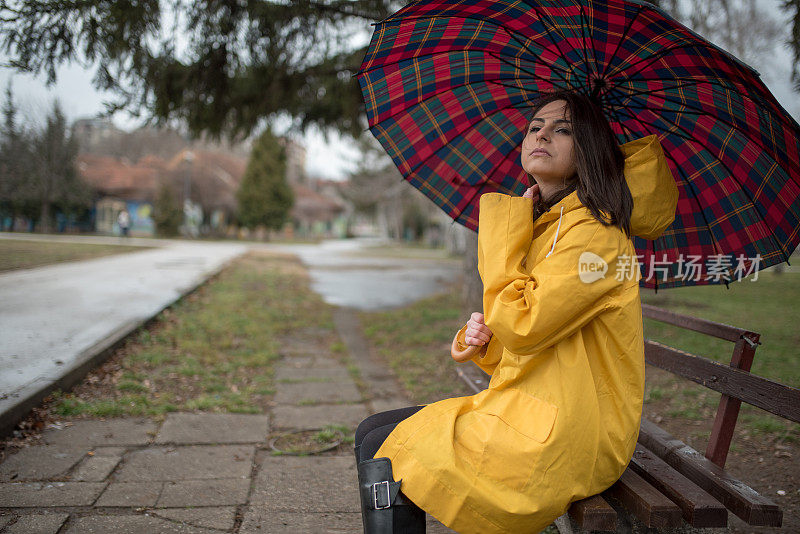 穿着黄色雨衣的年轻女子在公园里度过雨天