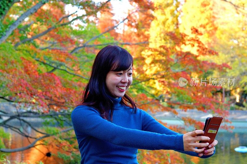 一名年轻的日本女子在东京井岛公园的秋叶下自拍