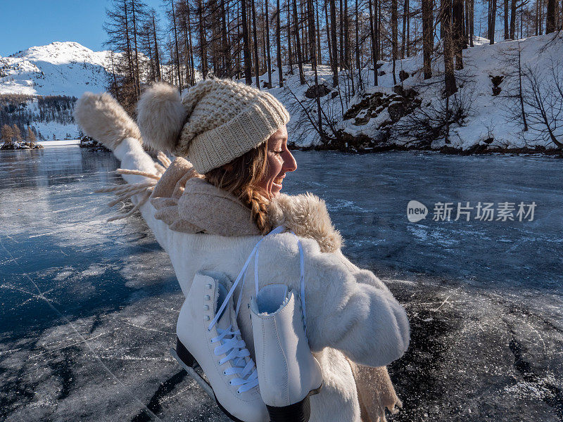 一个年轻女子肩上扛着冰鞋走在结冰的湖面上