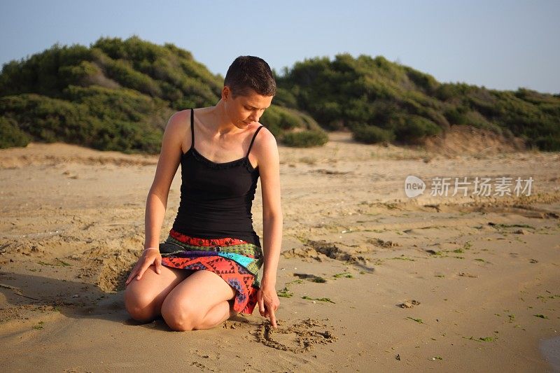 一个穿短裙的女人跪在沙滩上，在沙子上画一颗心