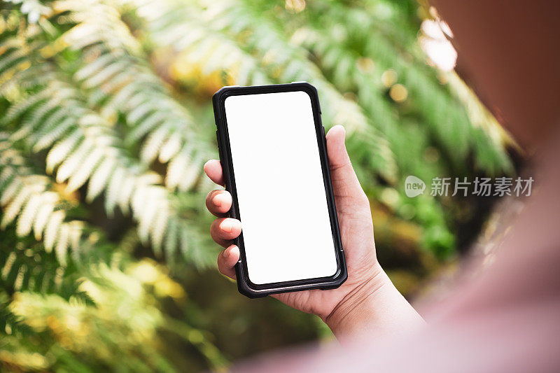 模拟图像的一个人持有白色空白屏幕智能手机与模糊的绿色自然背景。模拟手机。