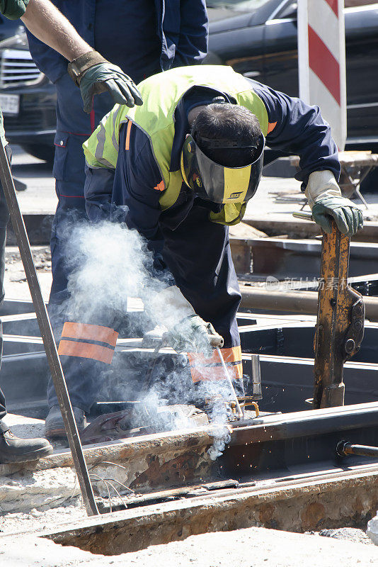焊接工在城市街道十字路口工作，用新铁轨替换旧铁轨并进行电弧焊接