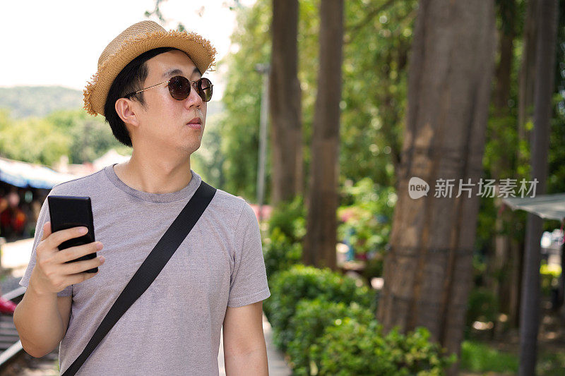 一名年轻的亚洲男子在火车站用手机上的地图导航。游客迷失在自然山