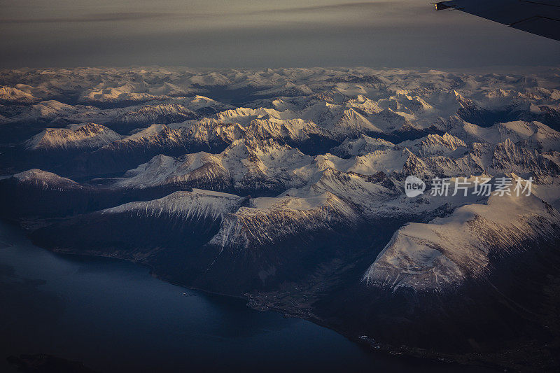 乘客从飞机上俯瞰挪威的北极峡湾，山上覆盖着积雪